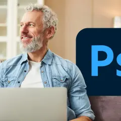 Uśmiechnięty mężczyzna z siwą brodą siedzi z laptopem, obok logo Photoshop. Dowiedz się, psd co to jest i jak go używać.