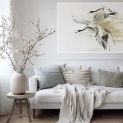 Biała sofa z poduszkami i narzutą, obok wazon z gałązkami kwitnącej wiśni. Na ścianie obraz z żurawiami, gdzie **negative space** podkreśla dynamikę ptaków.
