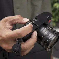 Dłoń trzyma czarny aparat fotograficzny z obiektywem.