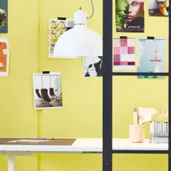 Inspirujący moodboard na żółtej ścianie: inspiracje modowe, graficzne i materiałowe. Obok biurko z narzędziami do tworzenia.