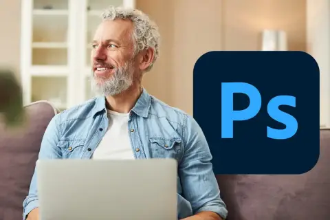 Uśmiechnięty mężczyzna z siwą brodą siedzi z laptopem, obok logo Photoshop. Dowiedz się, psd co to jest i jak go używać.