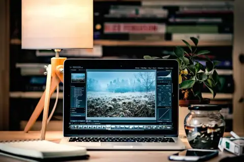 Laptop z edytorem zdjęć, na ekranie zimowy krajobraz. Obok lampka, notatnik i słoik z przetworami. To idealne miejsce do pracy nad plikami tif.
