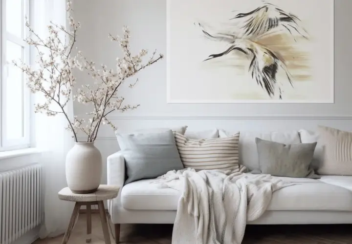 Biała sofa z poduszkami i narzutą, obok wazon z gałązkami kwitnącej wiśni. Na ścianie obraz z żurawiami, gdzie **negative space** podkreśla dynamikę ptaków.