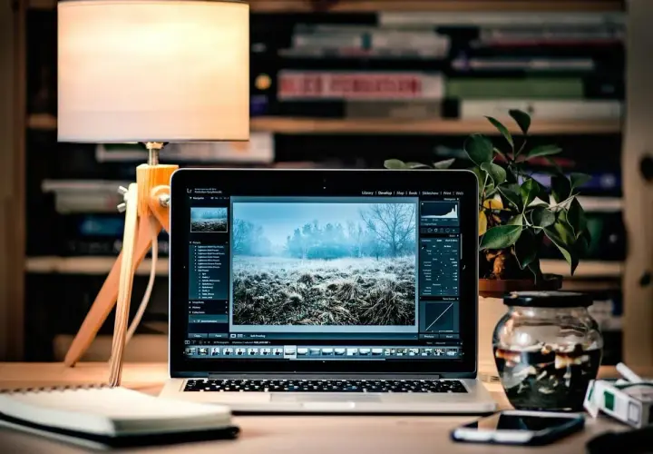 Laptop z edytorem zdjęć, na ekranie zimowy krajobraz. Obok lampka, notatnik i słoik z przetworami. To idealne miejsce do pracy nad plikami tif.