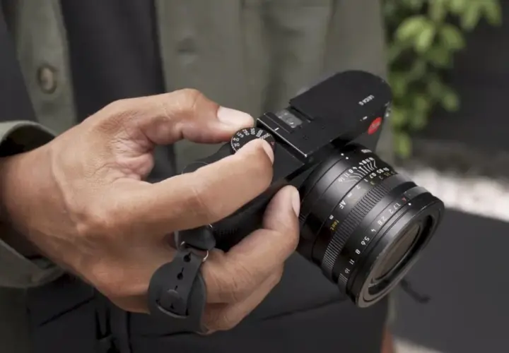 Dłoń trzyma czarny aparat fotograficzny z obiektywem.